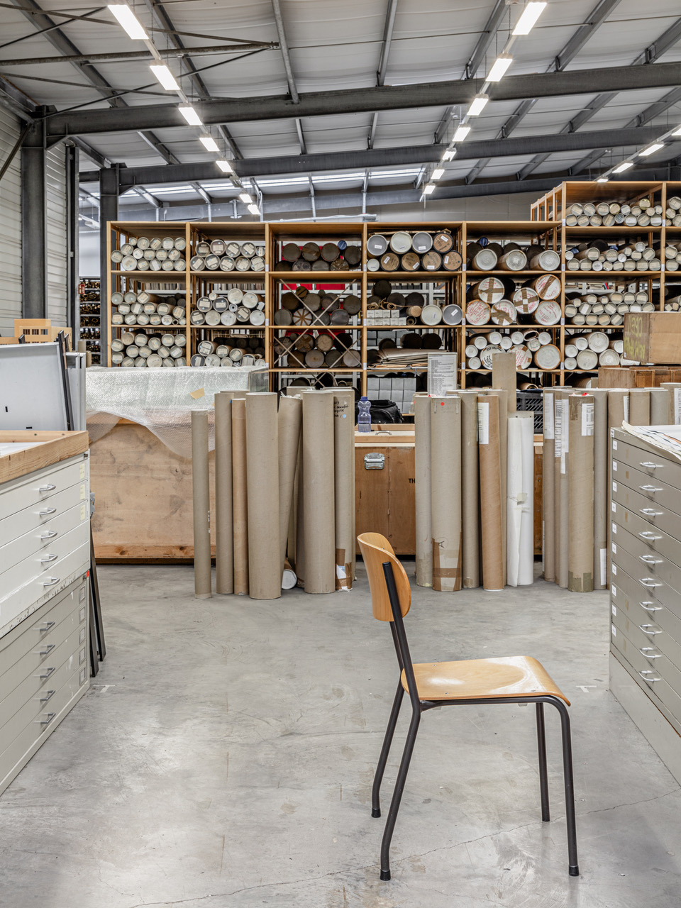 Arbeitswerkstatt mit Regalreisern, Rohre und Rollen, einsamer Stuhl im Vordergrund.